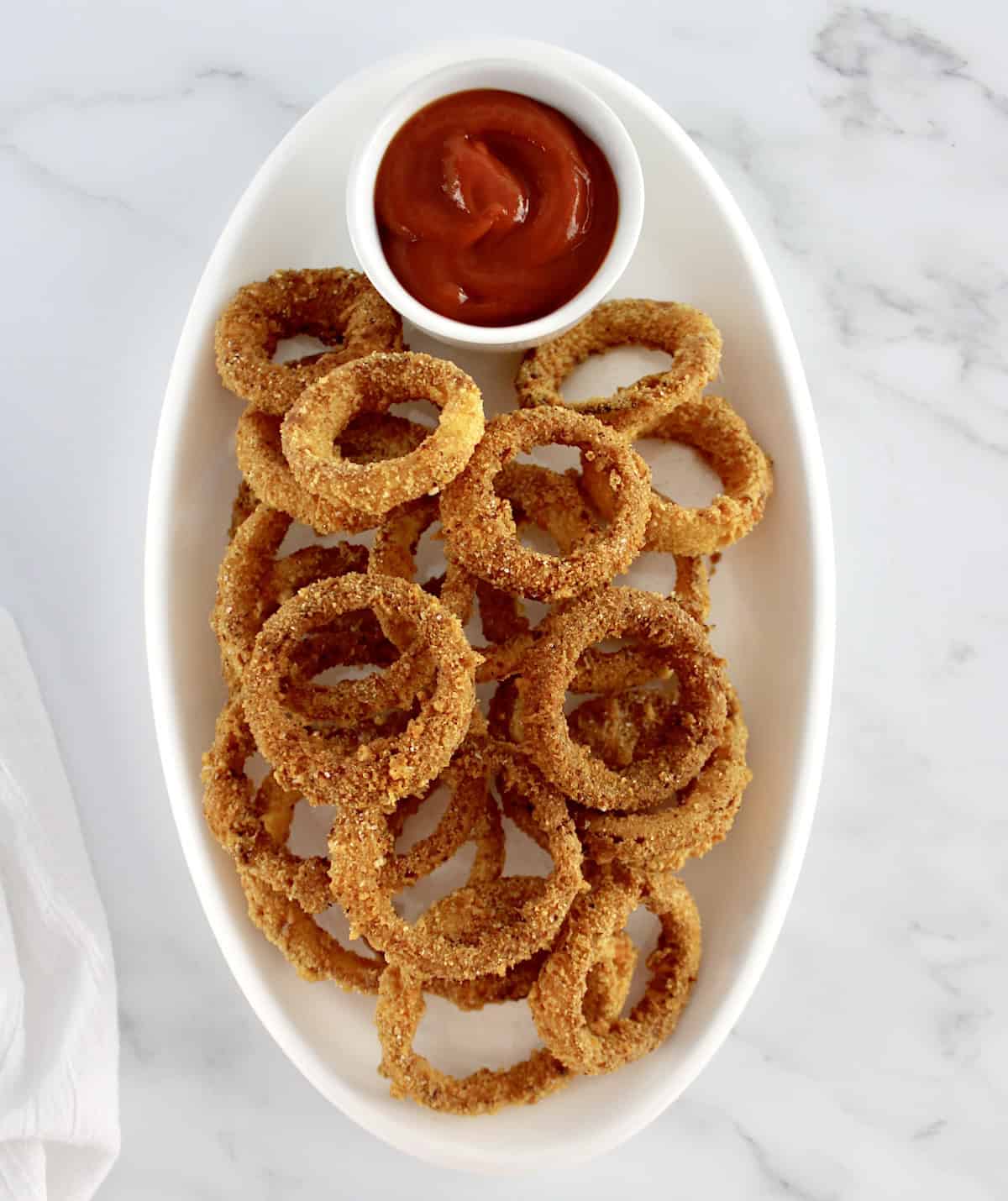 overhead view of Air Fryer Onion Rings on white oval platter with cup of ketchup