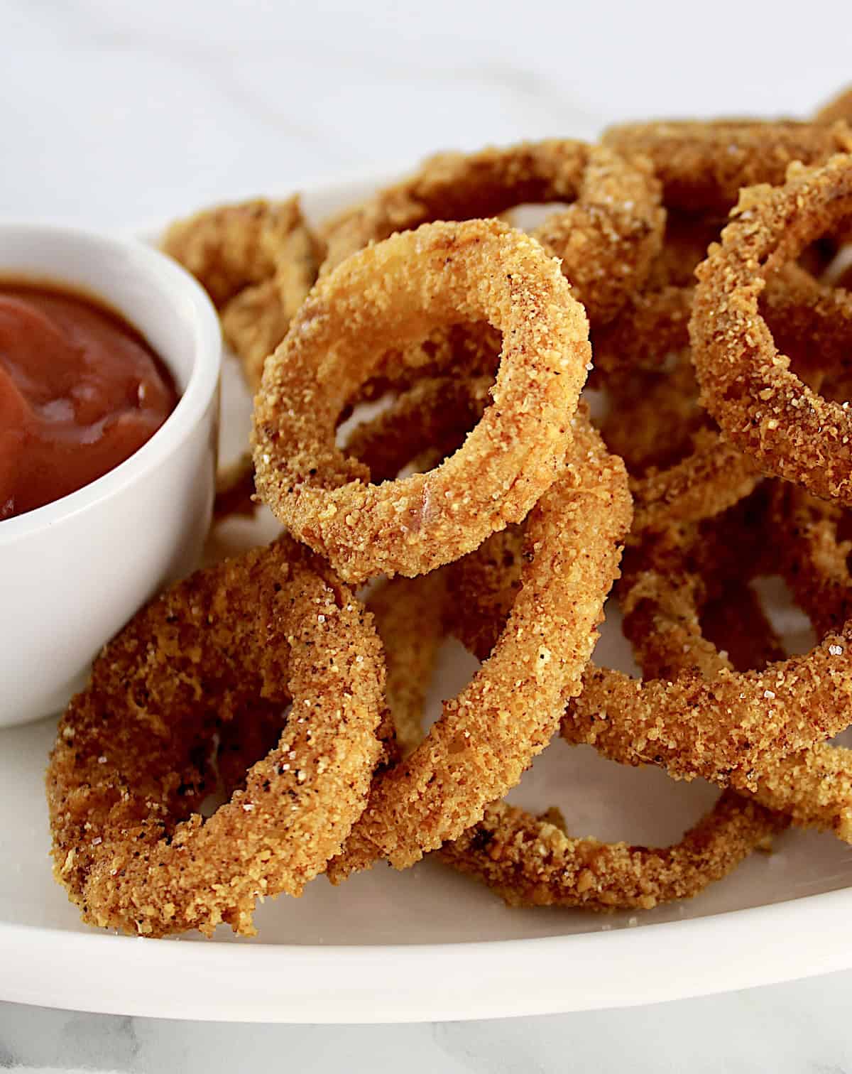 Air Fryer Onion Rings on white platter with white cup of ketchup on side