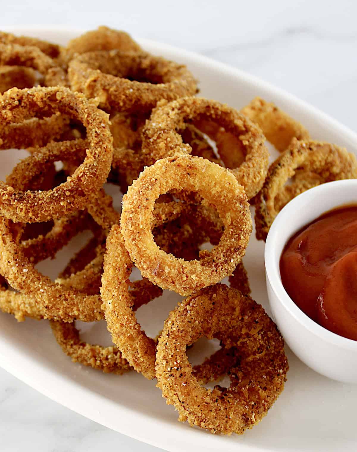 Air Fryer Onion Rings on white platter with white cup of ketchup on side