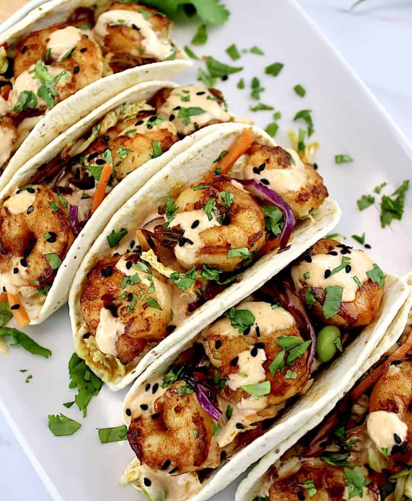 asian shrimp tacos on white plate with yum yum sauce drizzled on top