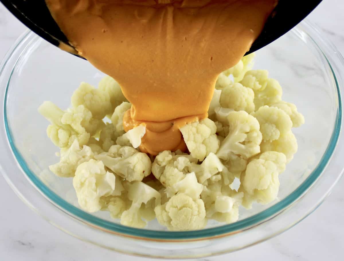 Buffalo Cauliflower Mac and Cheese being poured over cooked cauliflower florets in glass bowl