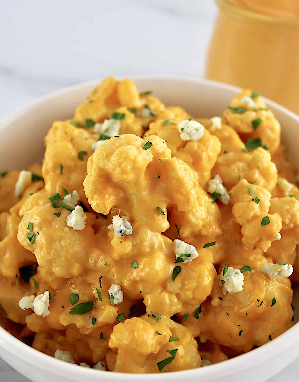 Buffalo Cauliflower Mac and Cheese in white bowl with sauce in glass jar in back