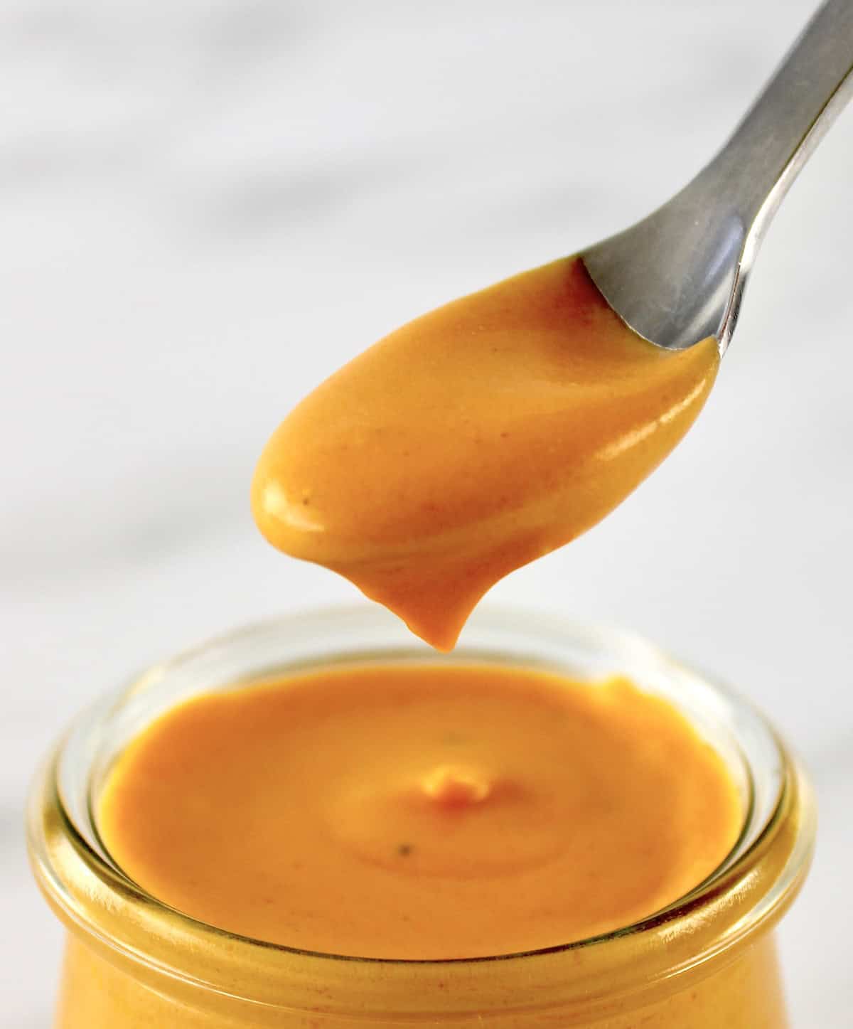 Buffalo Cheese Sauce and Dip dripping off spoon held over open glass jar