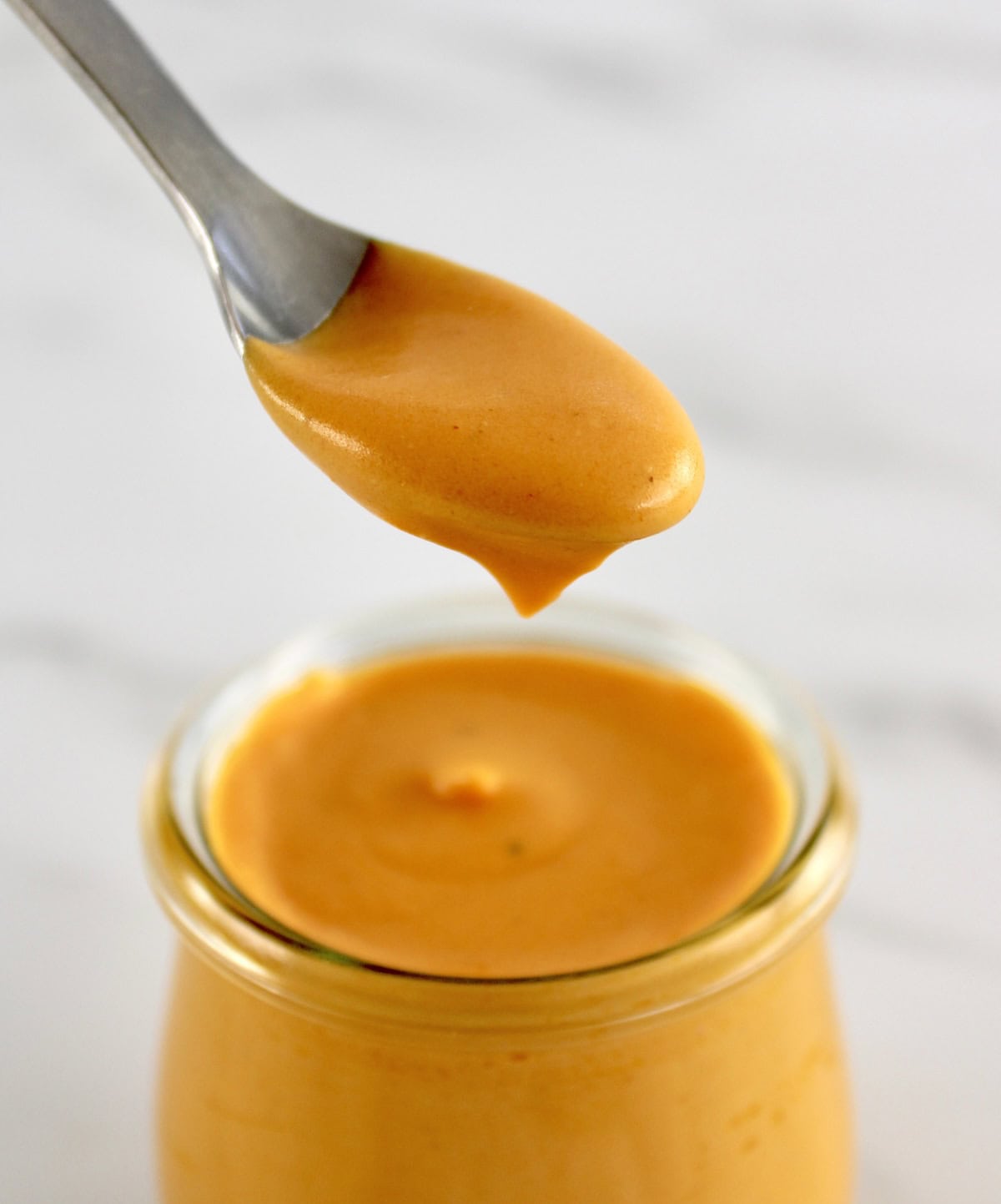 Buffalo Cheese Sauce and Dip dripping off spoon held over open glass jar