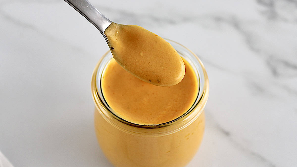 Buffalo Cheese Sauce and Dip in spoon held over open glass jar