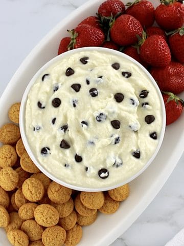 Cannoli Dip in white bowl with cookies and strawberries on side