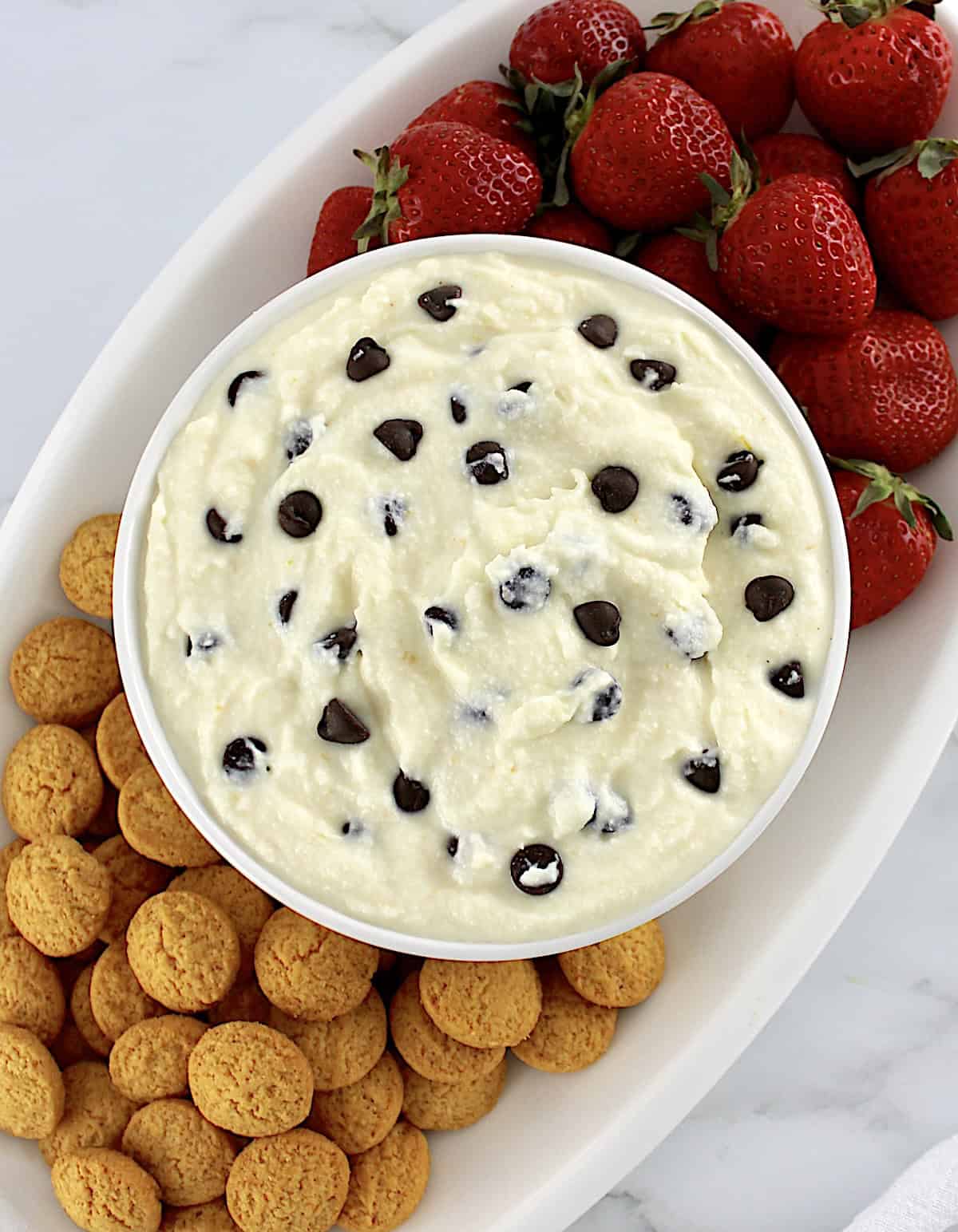 Cannoli Dip in white bowl with cookies and strawberries on side