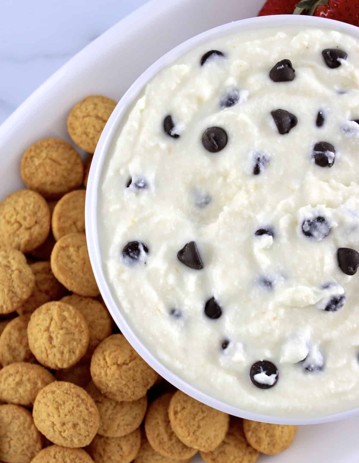 closeup of Cannoli Dip in white bowl with chocolate chips and vanilla wafers on side