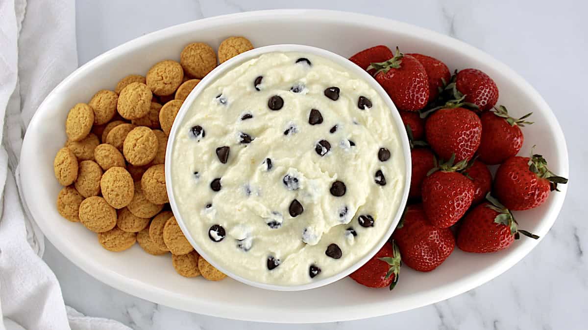 Cannoli Dip in white bowl with strawberries and vanilla wafers on side