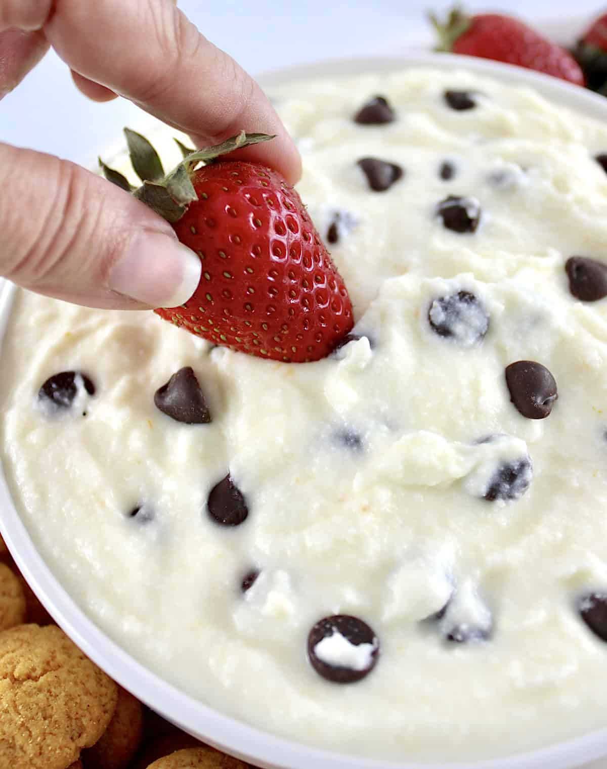 strawberry dipping into Cannoli Dip in white bowl with chocolate chips