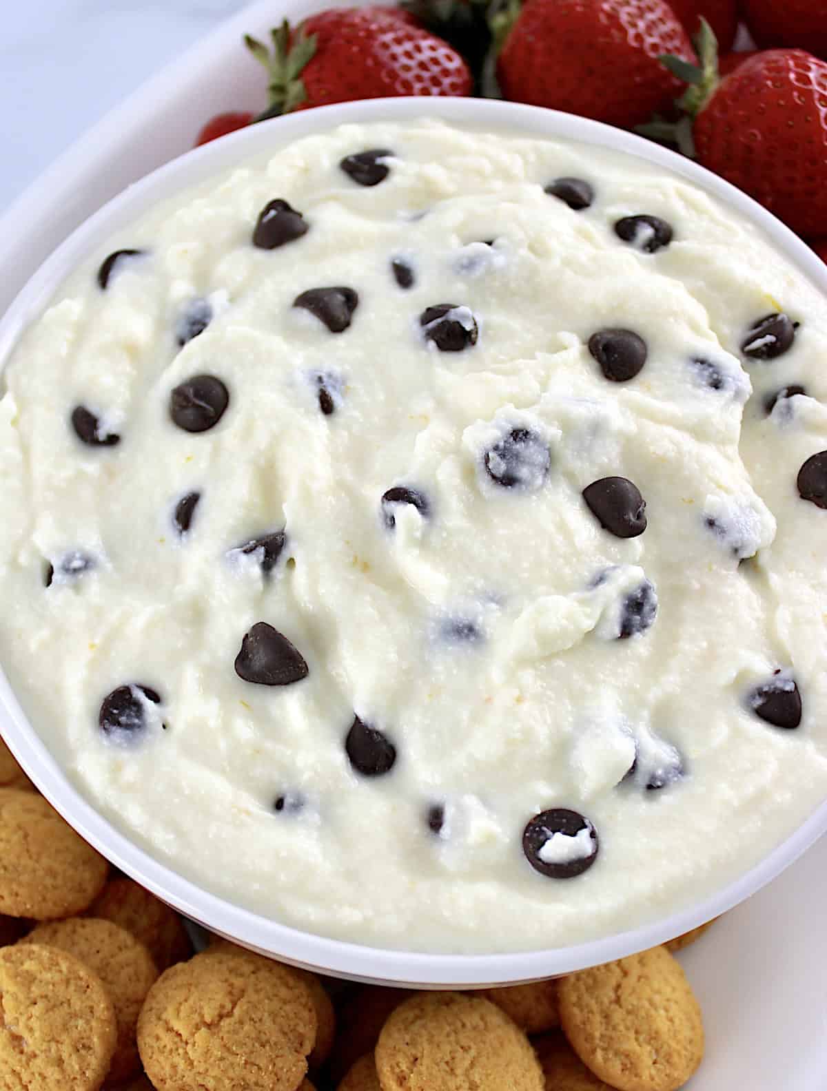 closeup of Cannoli Dip in white bowl with chocolate chips and strawberries and vanilla wafers on side