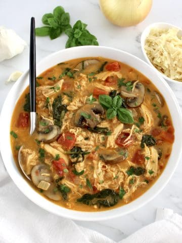 overhead view of Tuscan Chicken Soup in white bowl with spoon in it and fresh basil garnish