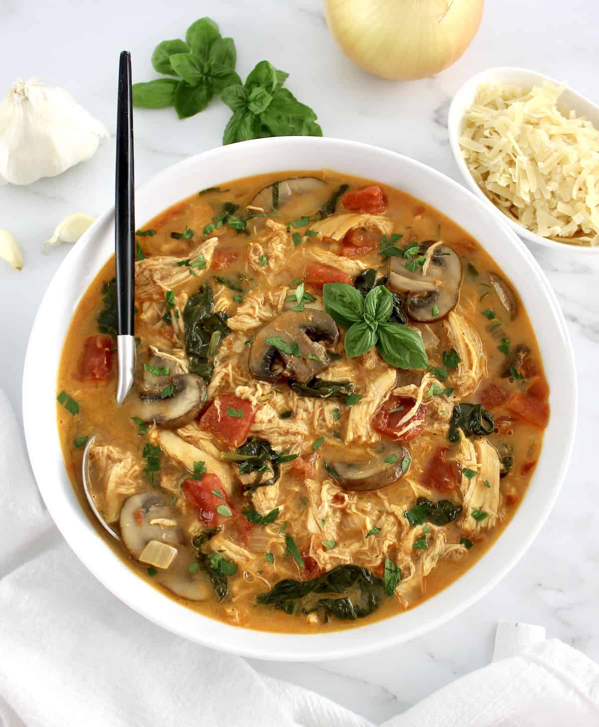 overhead view of Tuscan Chicken Soup in white bowl with spoon in it and fresh basil garnish