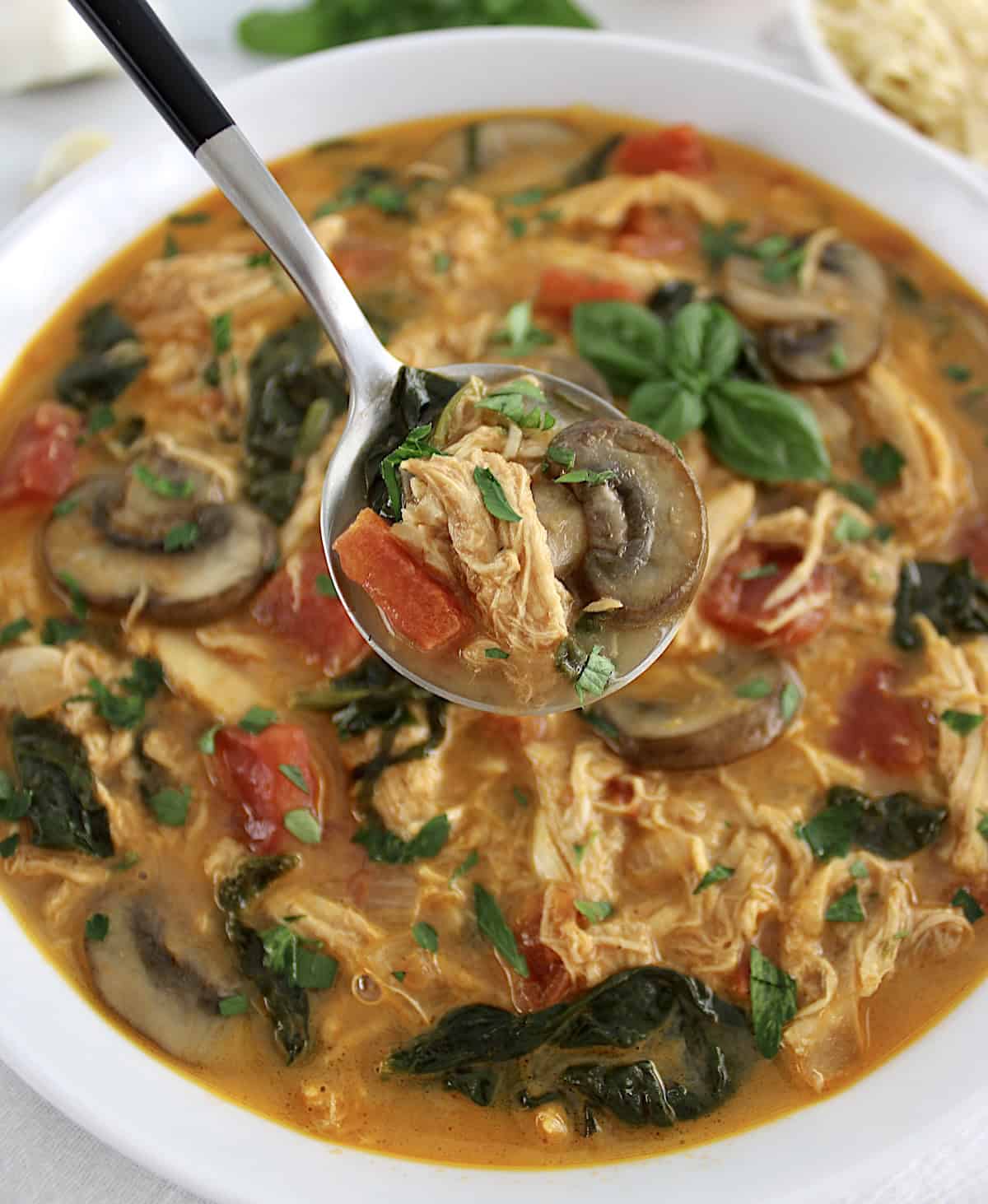 spoonful of Tuscan Chicken Soup held up over soup in white bowl