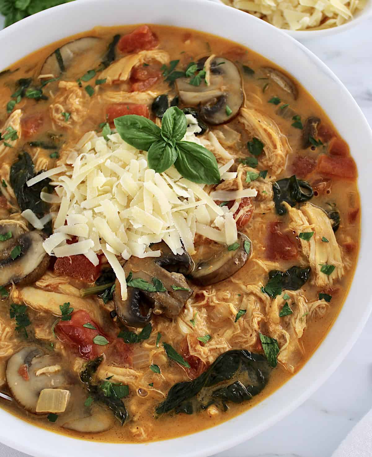 Tuscan Chicken Soup in white bowl with grated parmesan cheese and fresh basil leaves on top