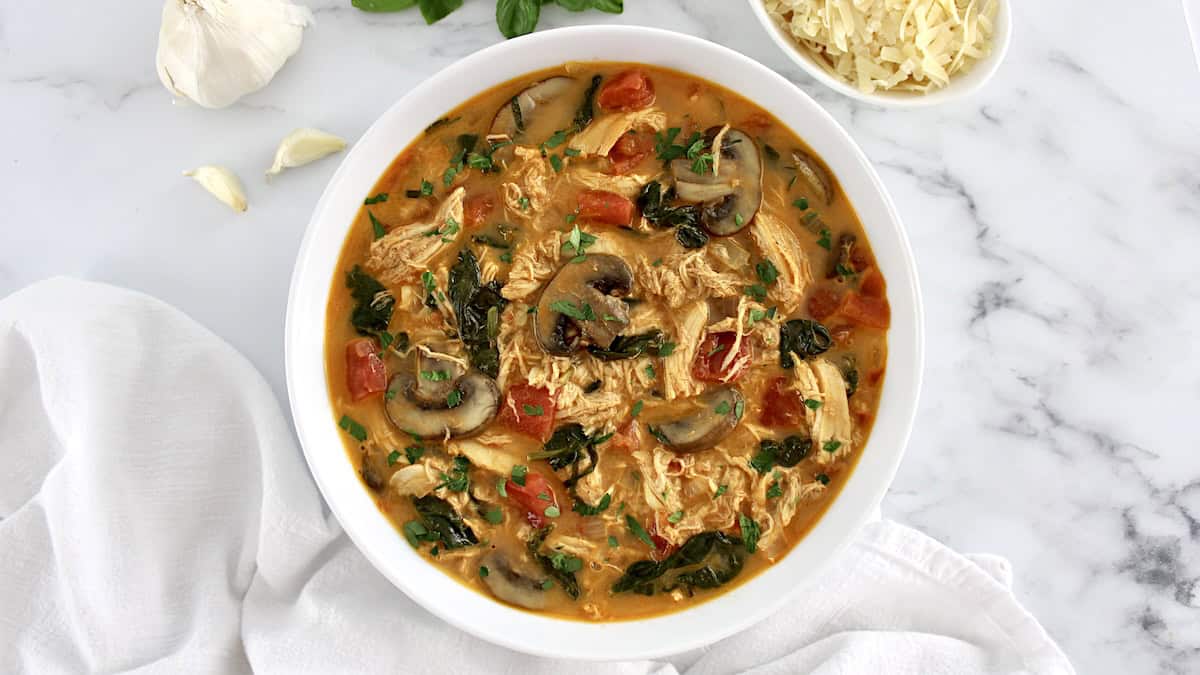 Tuscan Chicken Soup in white bowl with fresh basil garnish on top