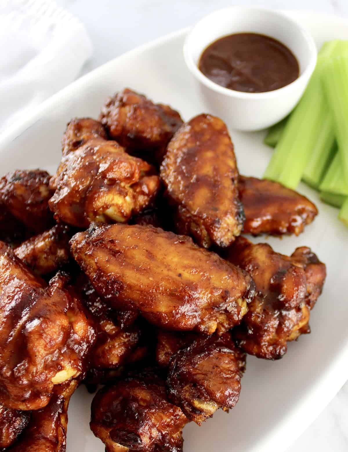 Honey BBQ Chicken Wings on white oval platter with bbq sauce and celery sticks