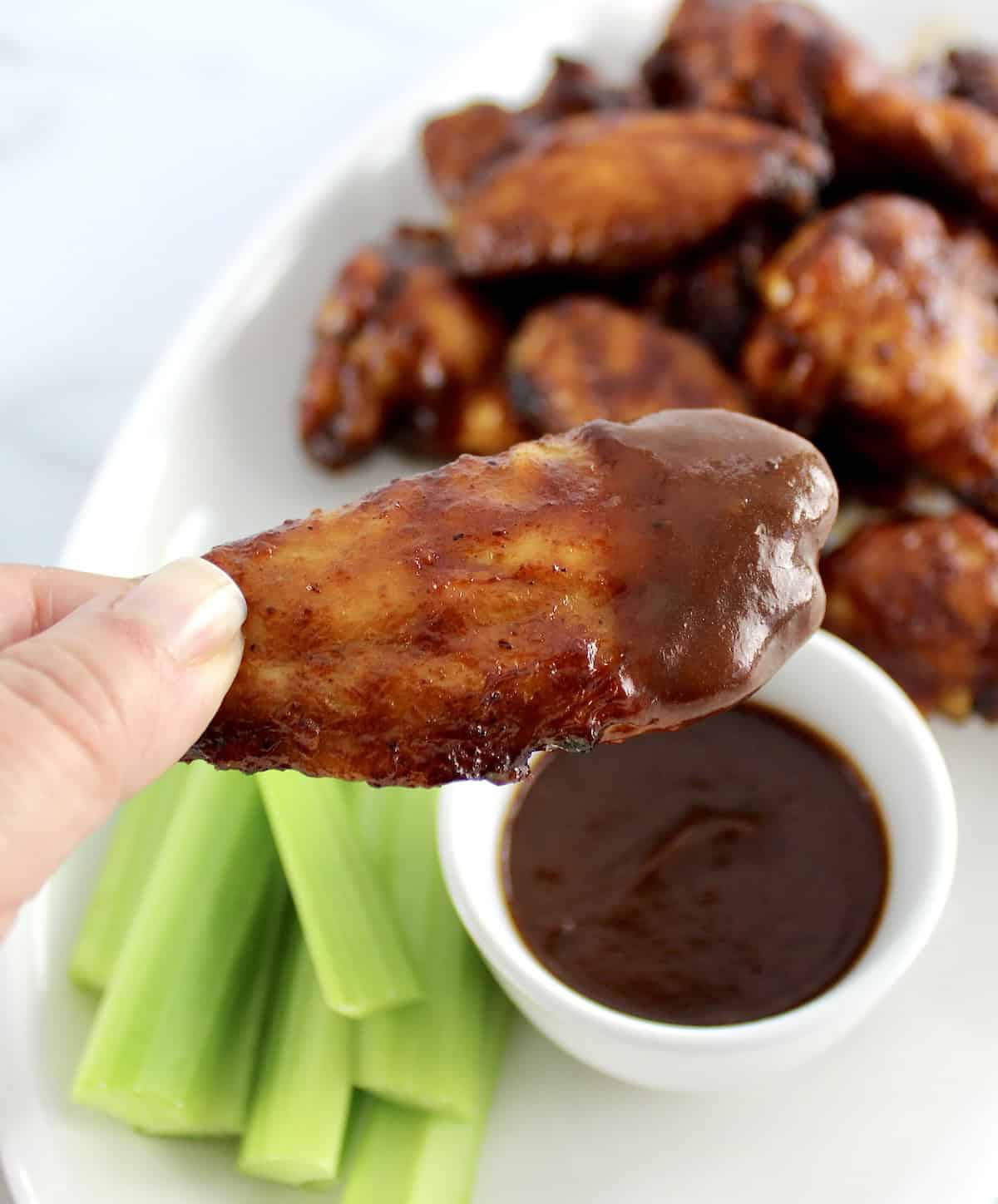 closeup of Honey BBQ Chicken Wing dipped in bbq sauce with more wings and celery in back