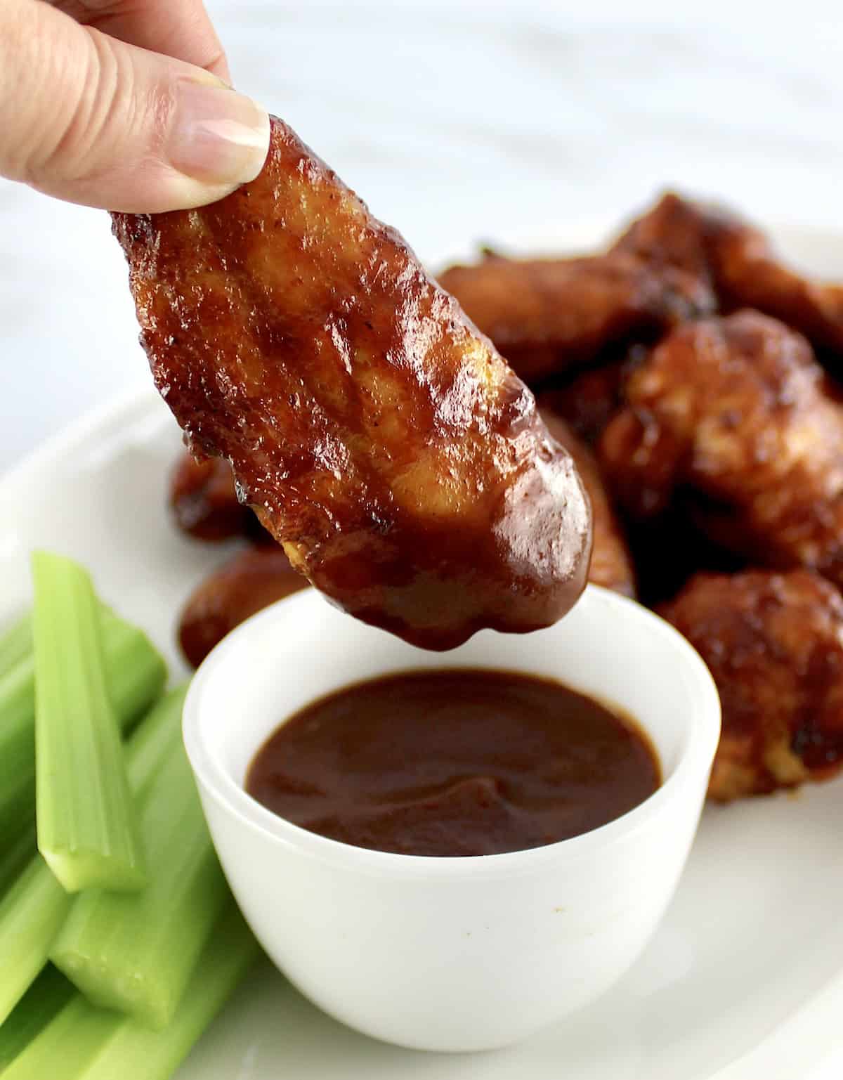 closeup of Honey BBQ Chicken Wing dipped in bbq sauce with more wings and celery in back