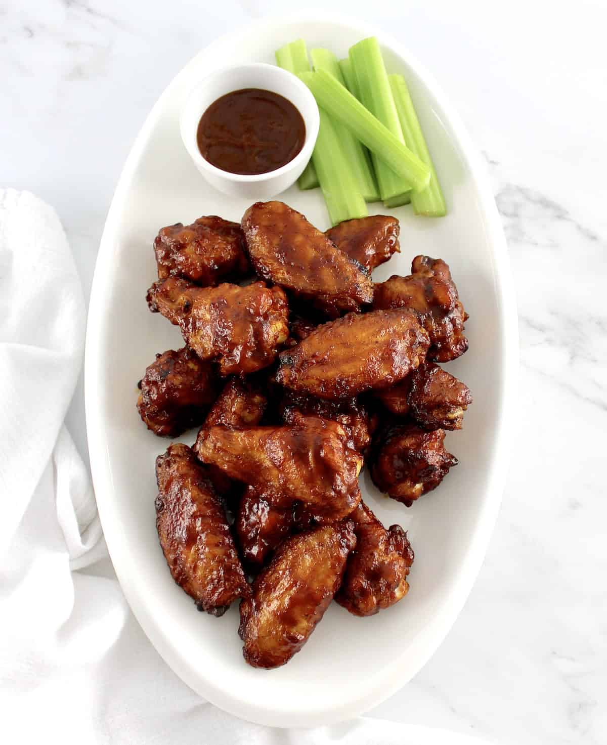 overhead view of Honey BBQ Chicken Wings on white oval plate with bbq sauce and celery