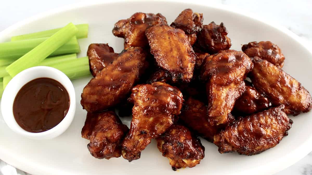 Honey BBQ Chicken Wings on white oval platter with bbq sauce and celery sticks