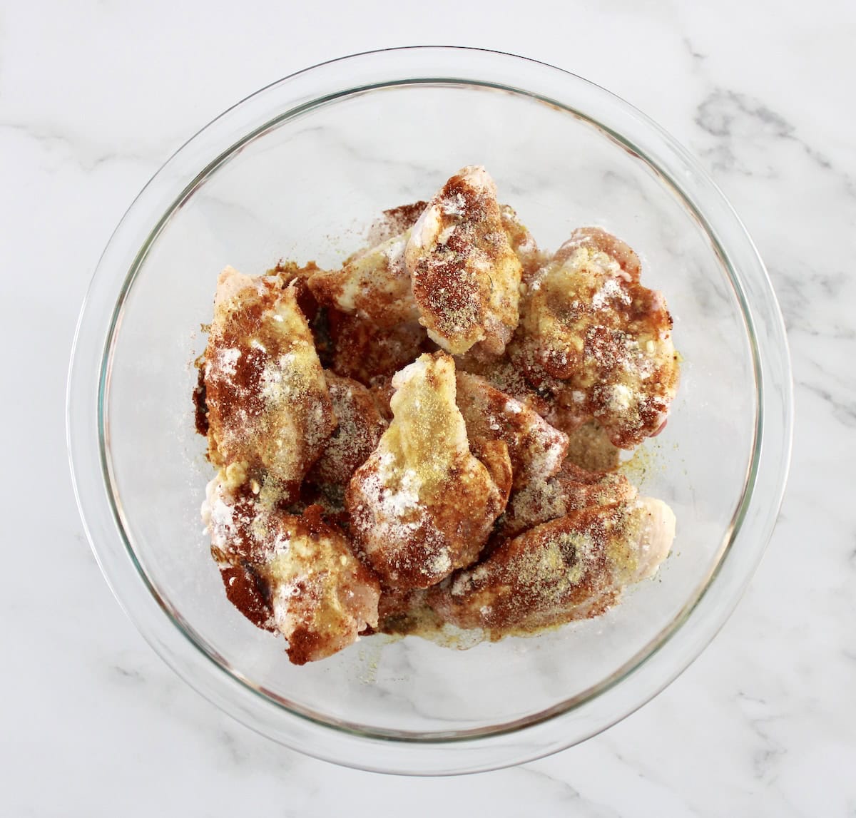 raw chicken wings with spices in glass bowl