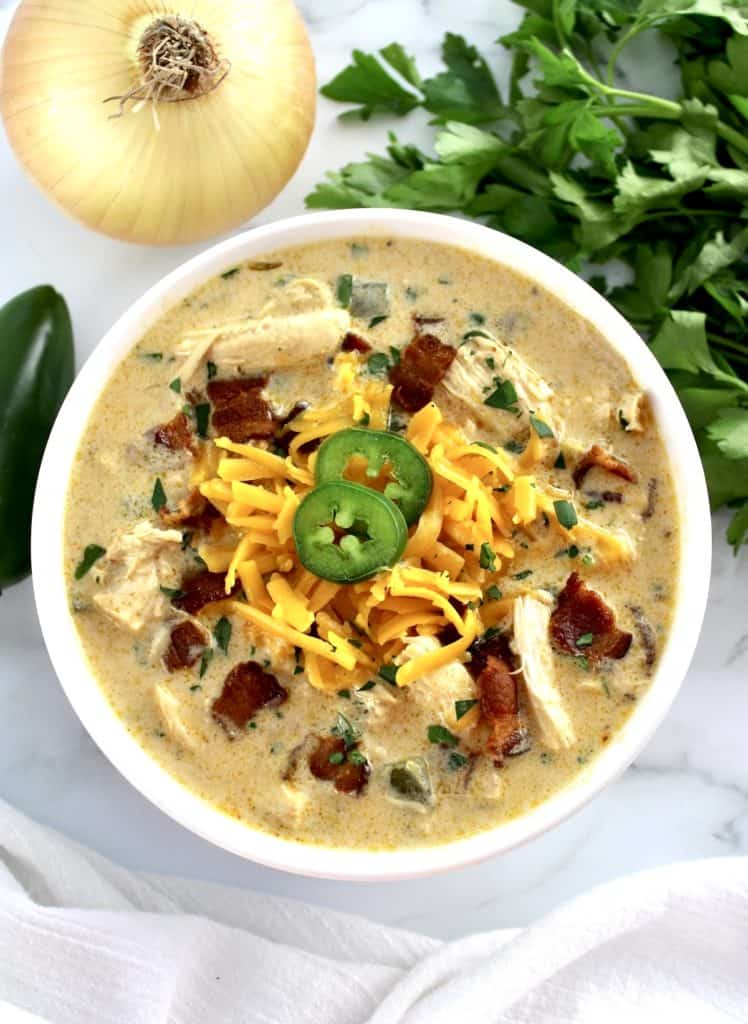 Jalapeño Popper Chicken Soup in white bowl with shredded cheddar and 2 pepper slices on top