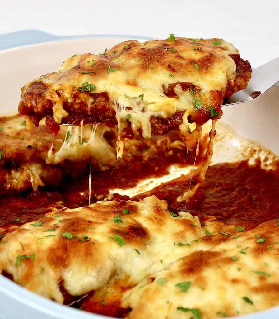 Chicken Parmesan piece being held up by silver spatula with cheese pull