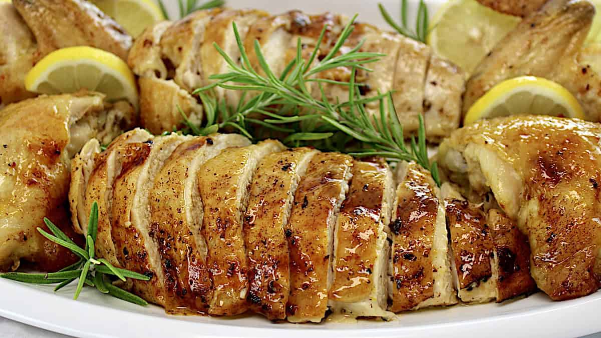 Oven Roasted Chicken sliced on white platter with fresh rosemary and lemon slices