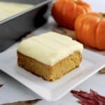 slice of Pumpkin Spice Cake on white plate with pumpkins and baking pan in background