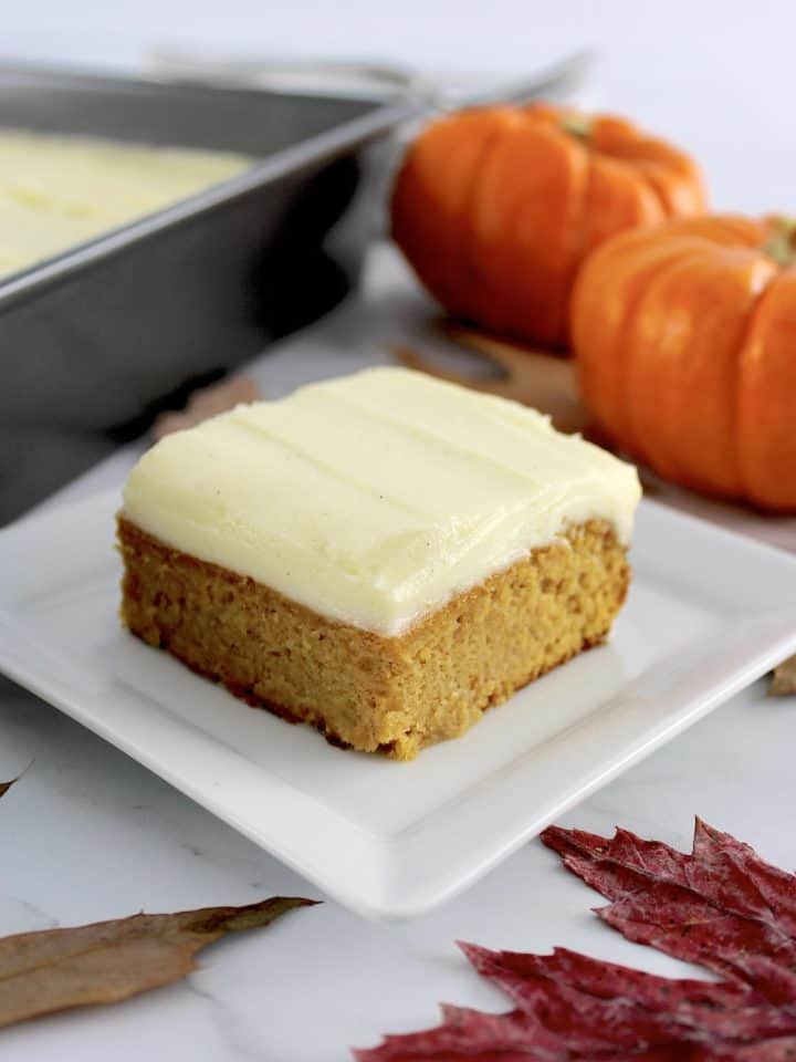 slice of Pumpkin Spice Cake on white plate with pumpkins and baking pan in background