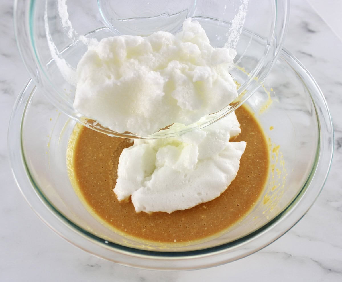 Pumpkin Spice Cake wet ingredients in glass bowl with whipped egg whites being poured in