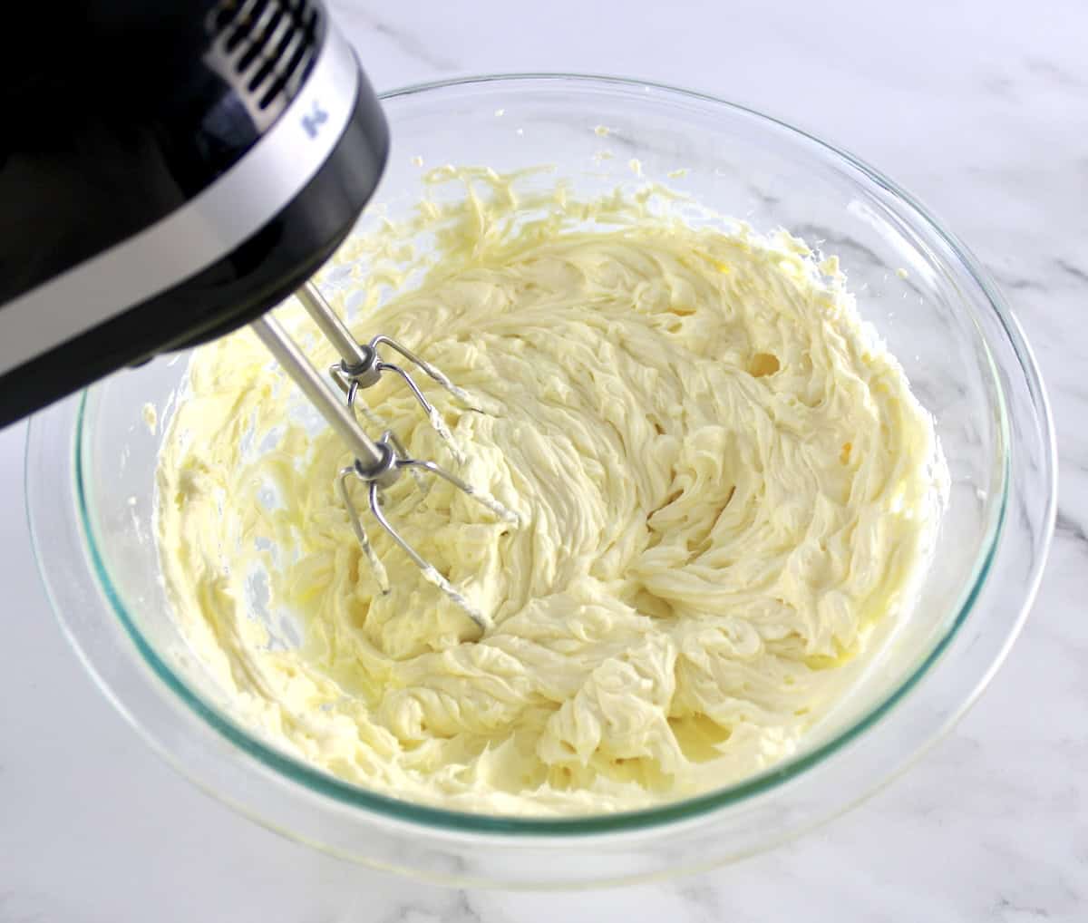 cream cheese and butter being whipped in glass bowl with hand mixer