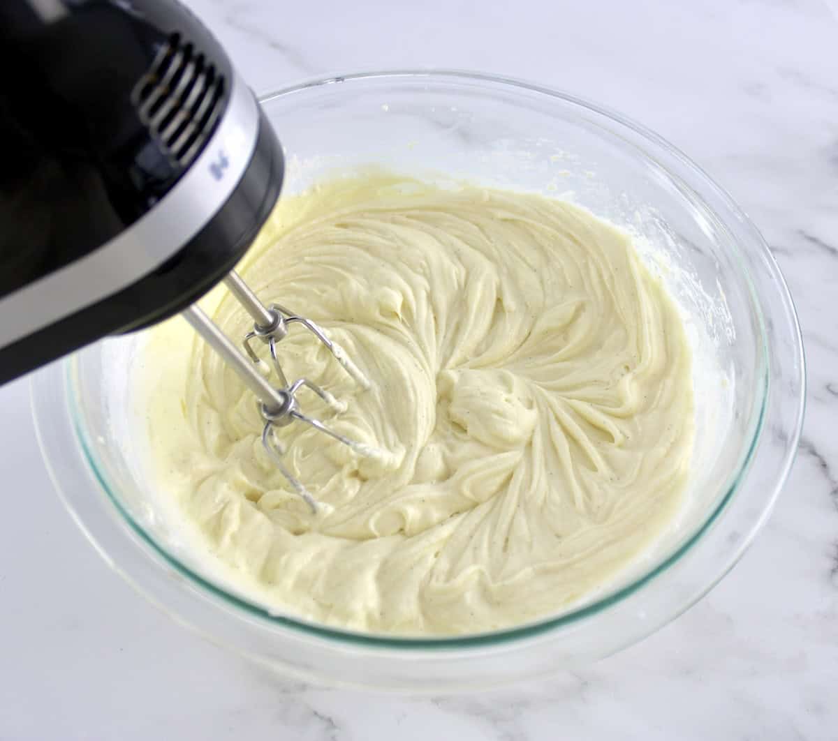 Pumpkin Spice Cake frosting being whipped in glass bowl with hand mixer