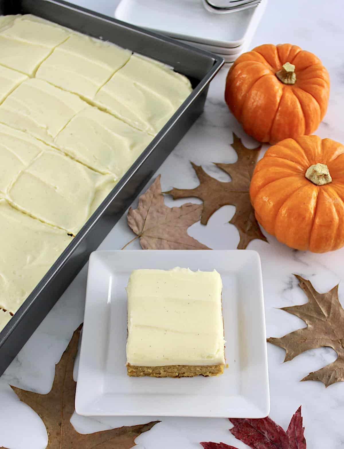 Pumpkin Spice Cake slice on white plate with cake pan and pumpkins in back