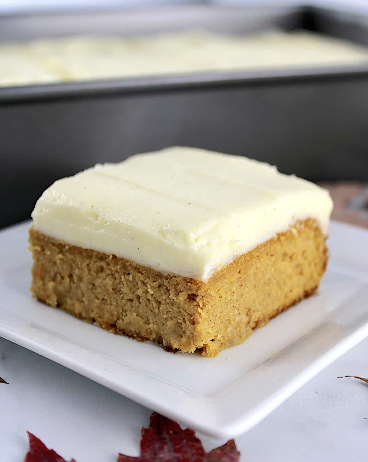 closeup of slice of Pumpkin Spice Cake on white plate with baking pan in back