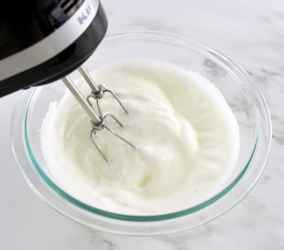 egg whites being whipped with hand mixer in glass bowl