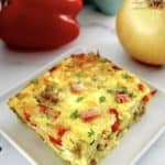 slice of Sausage and Peppers Breakfast Casserole on white plate with red pepper and onion in back