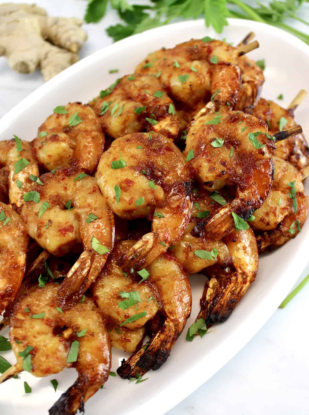 Air Fryer Asian Shrimp Skewers stacked up on white oval platter with chopped parsley on top