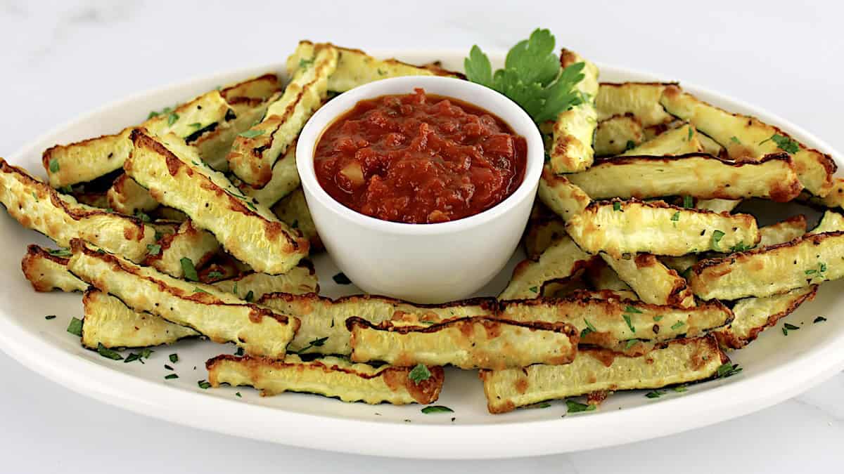 Baked Parmesan Zucchini Fries on white oval plate with marinara sauce in cup in center