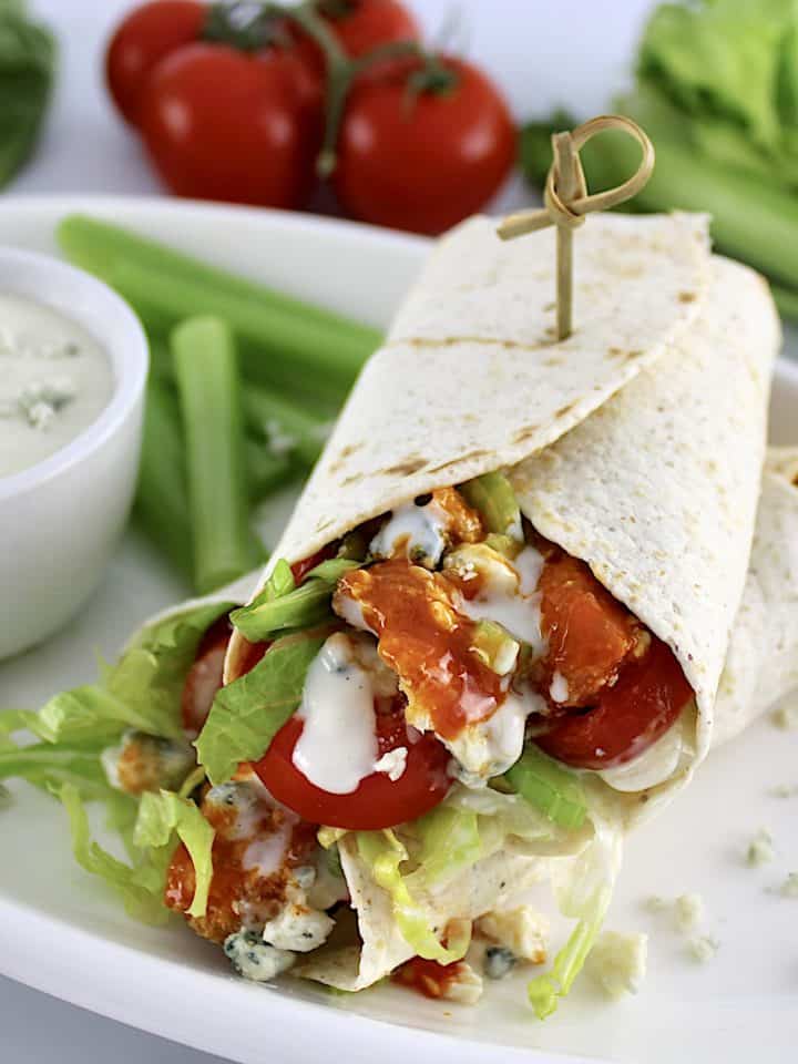 Buffalo Chicken Wrap cut in half on white plate with blue cheese and celery sticks on side