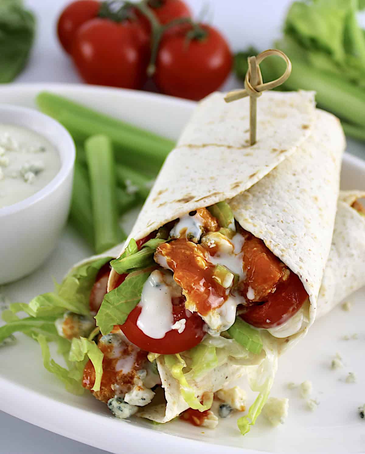 Buffalo Chicken Wrap cut in half on white plate with blue cheese and celery sticks on side