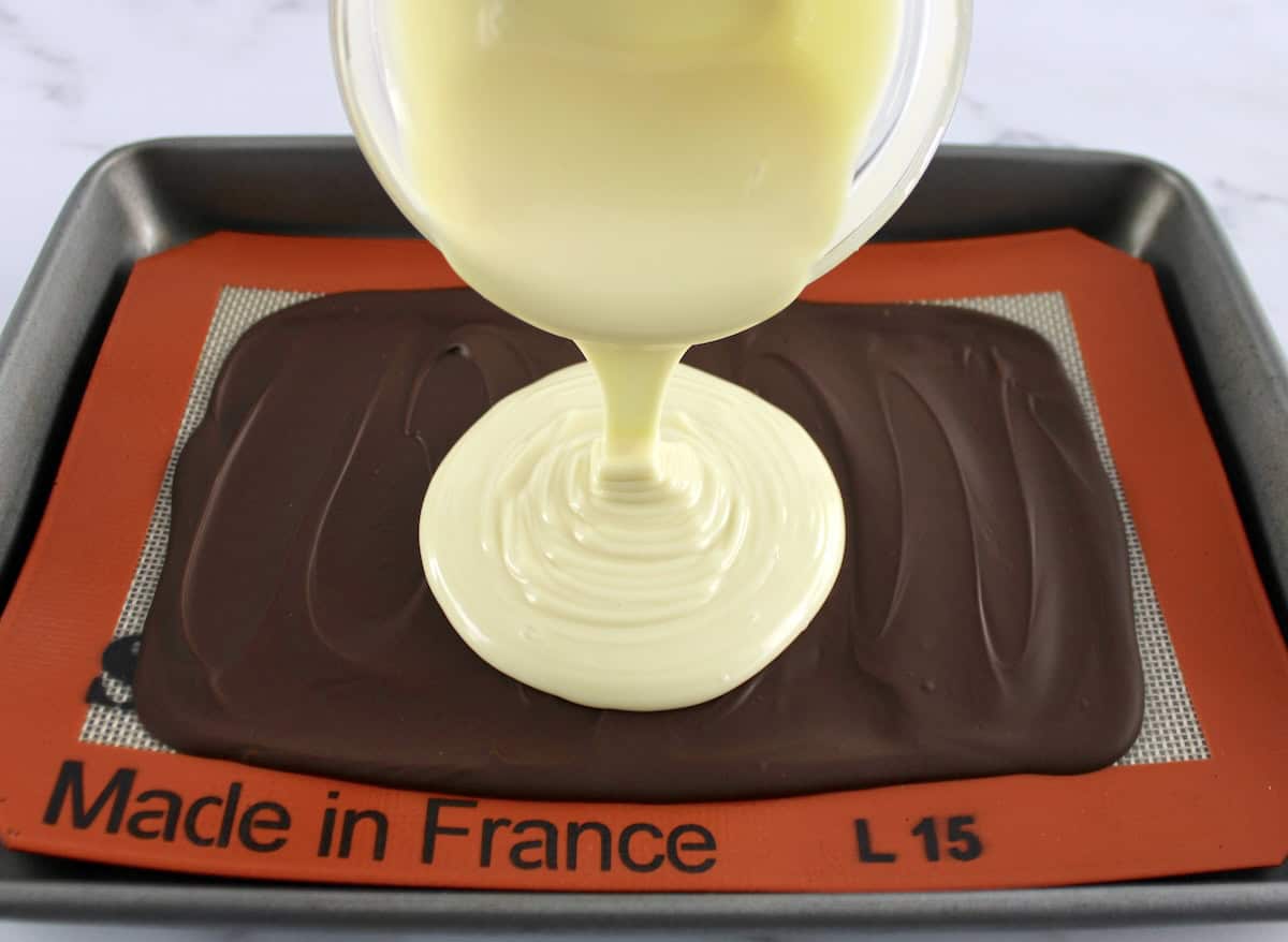 melted white chocolate being poured over milk chocolate on silpat lined baking sheet