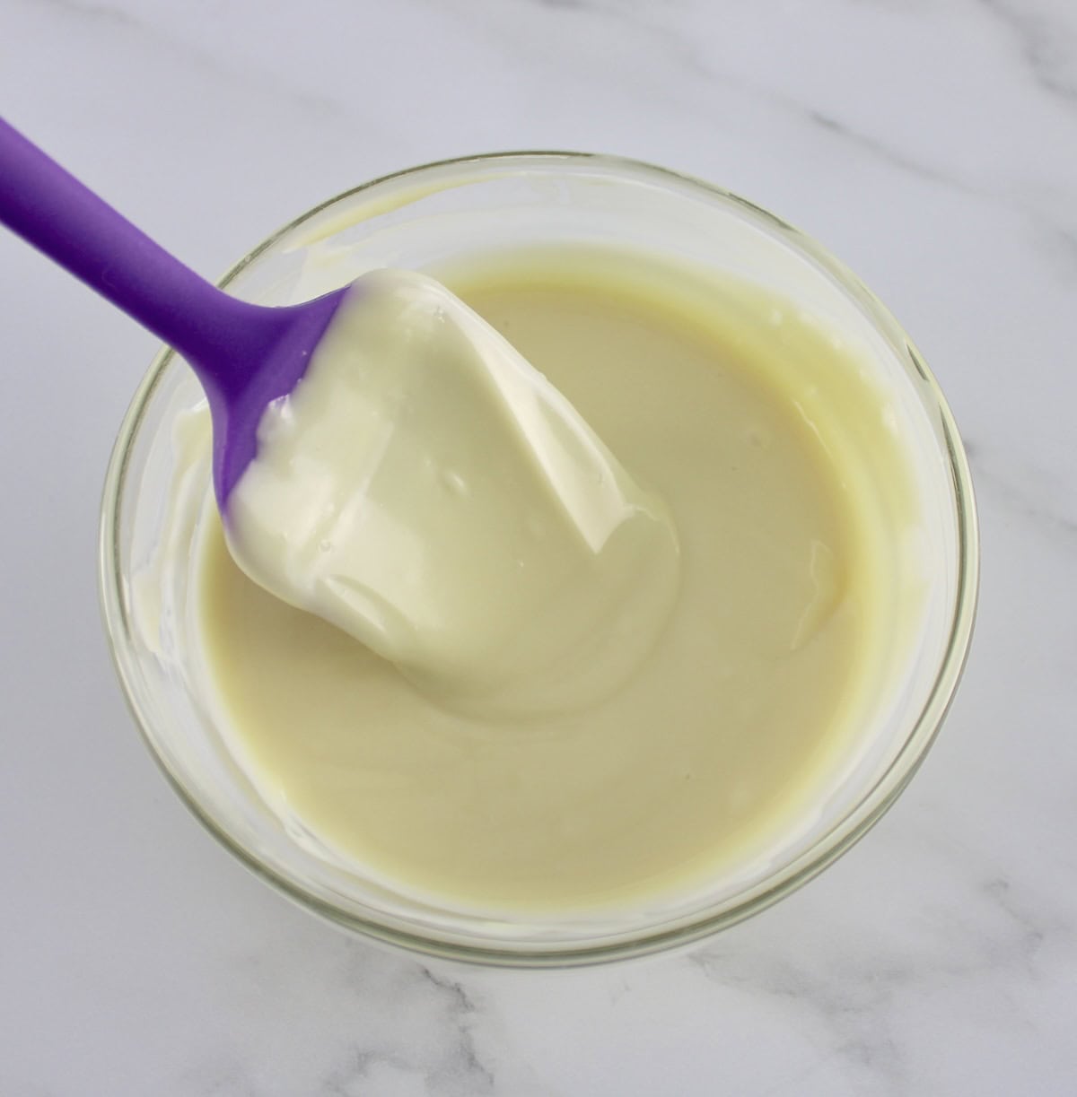 melted white chocolate in glass bowl with purple spatula