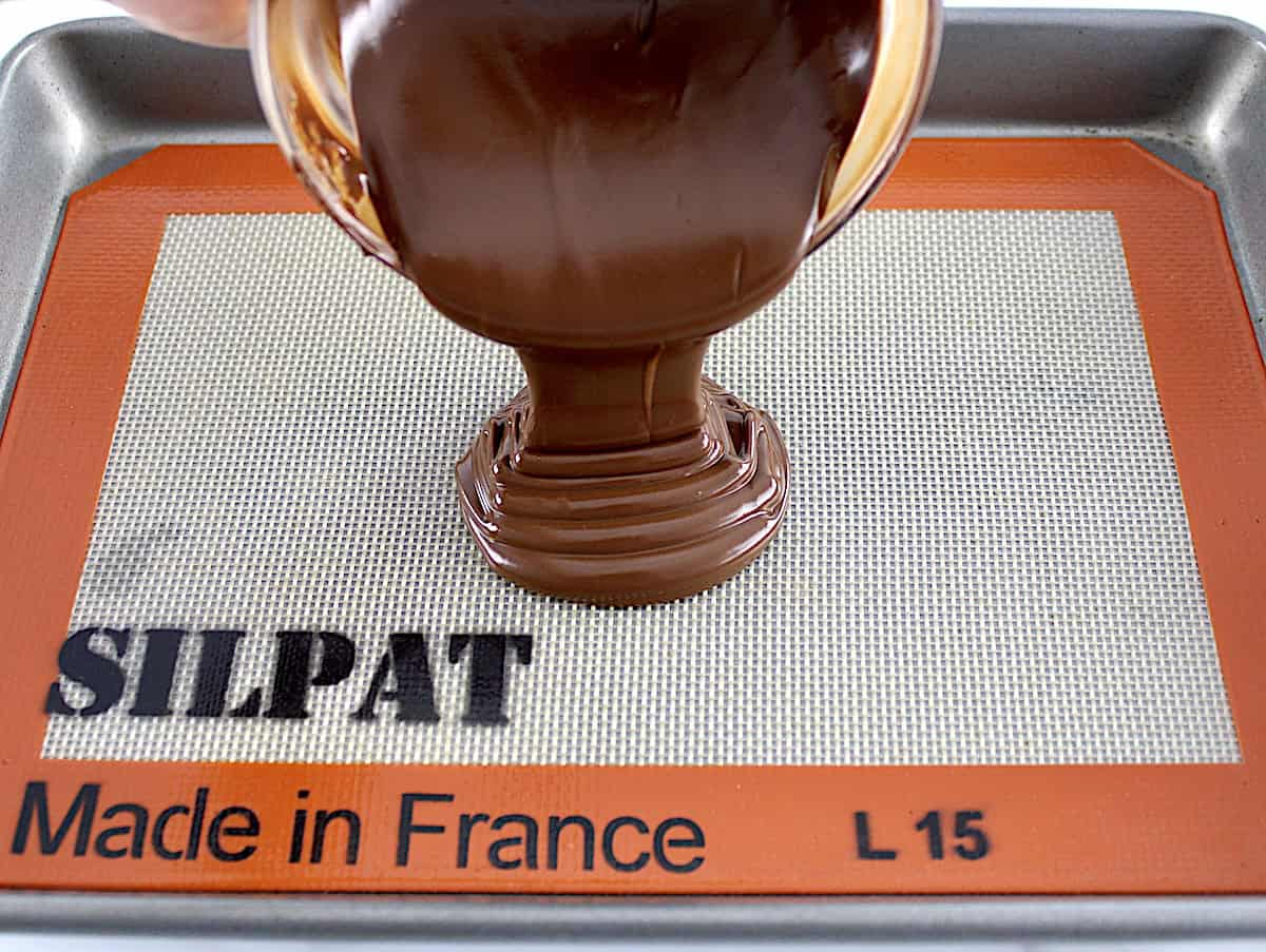 melted chocolate being poured onto silpat lined baking sheet