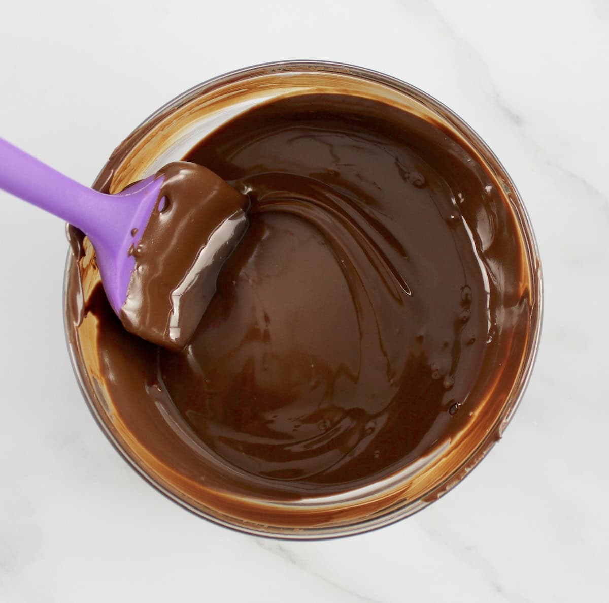 melted chocolate in glass bowl with purple spatula