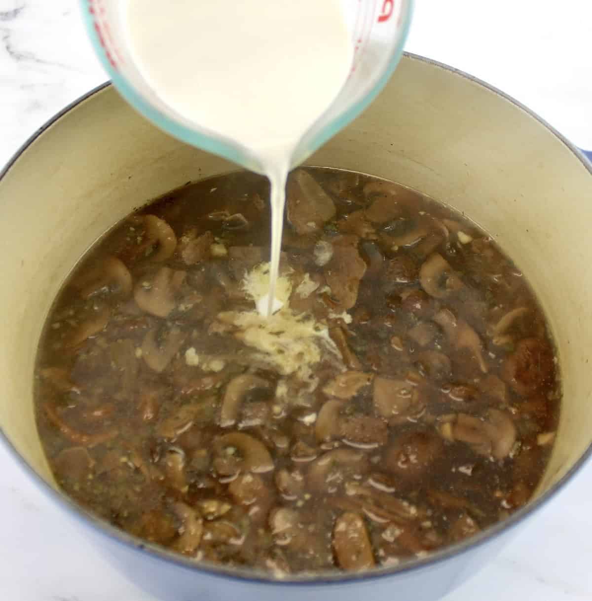 heavy cream being poured into dutch oven with Cream of Wild Mushroom Soup