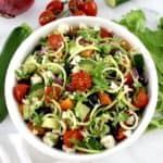 overhead view of Greek Zucchini Pasta Salad in white bowl with veggies in back