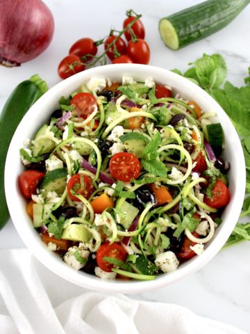 overhead view of Greek Zucchini Pasta Salad in white bowl with veggies in back