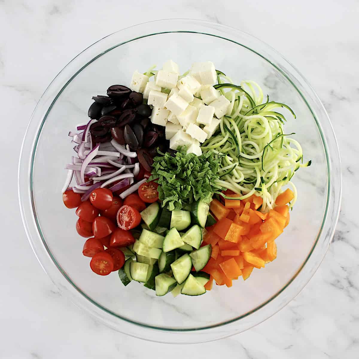 Greek Zucchini Pasta Salad ingredients in glass bowl in sections unmixed